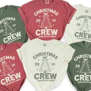 Könnte beinhalten: Sechs T-Shirts in verschiedenen Farben, darunter Grün, Rot und Creme. Jedes Shirt zeigt den Text "CHRISTMAS 20 25 CREW" mit einem Weihnachtsbaum-Motiv. Der Satz "Making Memories Together" ist unter dem Wort "CREW" gedruckt.