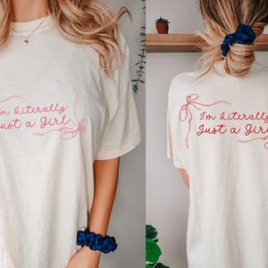 Może przedstawiać: Kremowy t-shirt z napisem "I'm Literally Just a Girl" w różowym skrypcie. Projekt znajduje się z przodu i z tyłu koszulki. Codzienny, swobodny element garderoby.
