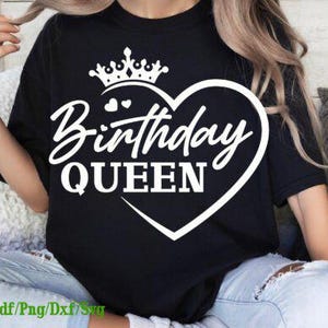 May include: Black t-shirt with a white heart-shaped design. The design includes a crown, the words "Birthday QUEEN" in a script font, and two small hearts. The shirt is worn by a person.