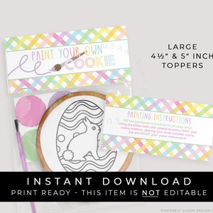 May include: A set of paint your own cookie kits featuring a bunny design. The kits include a 4 1/2 inch or 5 inch cookie, edible paint, and a paintbrush. The packaging is decorated with a colourful checkered pattern and the text "Paint Your Own Cookie".