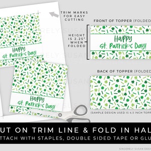 Puede incluir: Hoja impresa con dise&ntilde;os de adornos para tartas del D&iacute;a de San Patricio. Los adornos presentan una pancarta blanca con el texto "Happy St. Patrick's Day!" en verde, rodeada de tr&eacute;boles y virutas verdes. La altura plegada es de 5,7 cm.