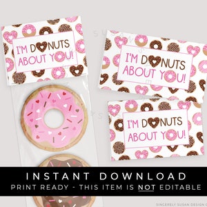 Op de afbeelding: Printbare donut-thema cadeaulabels met de tekst "I'm donuts about you!" in roze en bruin. De labels zijn versierd met roze en bruine donuts met roze harten.