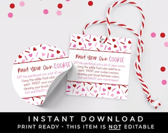 May include: A printable tag with a pink and red heart pattern and the text "Paint Your Own Cookie" with instructions for decorating cookies. The tag is attached to a red and white string.