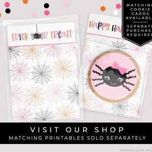 May include: A clear plastic bag with a pink and black spider cookie inside. The bag has a white label with the text "Trick or Treat!" and a spider web pattern. The bag is sitting on a white surface with a pink and orange spider web pattern.