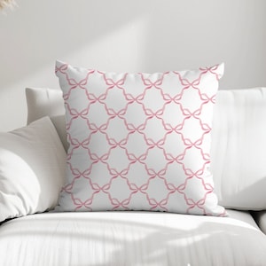 May include: A white throw pillow with a pink geometric pattern of interlocking loops. The pillow is on a white couch.