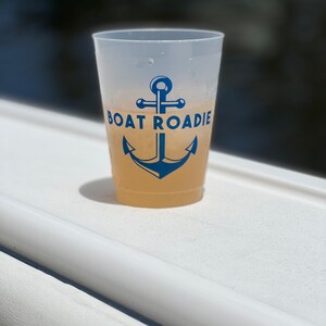 May include: A white plastic cup with a blue anchor and the text "BOAT ROADIE" printed on it. The cup is filled with a light yellow drink.
