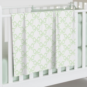 May include: A white crib sheet with a green bow pattern. The sheet is folded and draped over the crib.