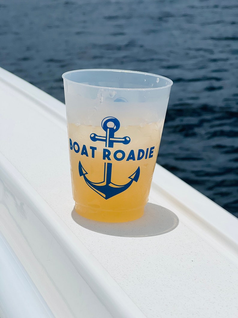 May include: A clear plastic cup with a yellow beverage and a blue anchor graphic with the text "Boat Roadie".