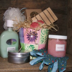 May include: A gift basket filled with bath and body products, including a bottle of body wash, a jar of sugar scrub, a tin of lotion, a loofah, and a pair of gardening gloves. The basket is decorated with pink and green floral patterns.