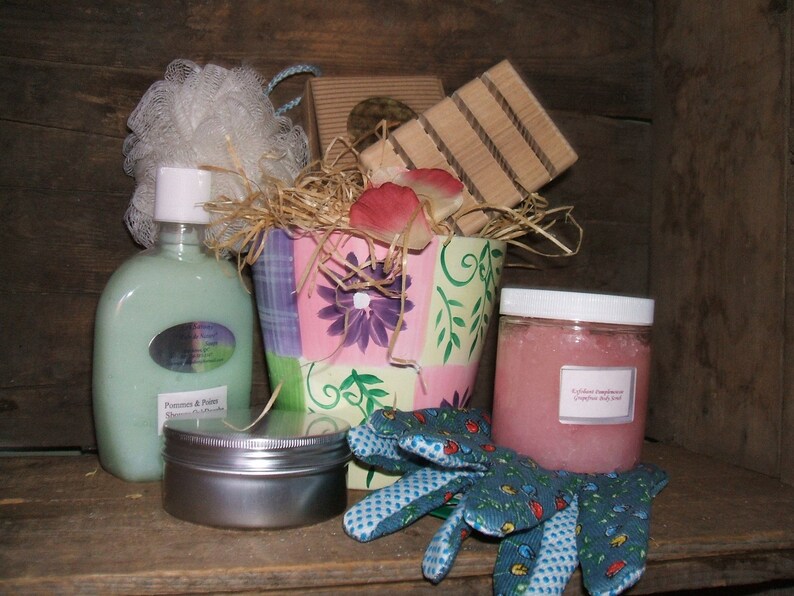May include: A gift basket filled with bath and body products, including a bottle of body wash, a jar of sugar scrub, a tin of lotion, a loofah, and a pair of gardening gloves. The basket is decorated with pink and green floral patterns.