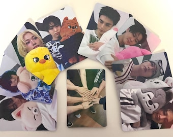 Puede incluir: Colección de tarjetas fotográficas hechas por fans con imágenes de un grupo musical, con miembros y peluches. Las tarjetas están dispuestas en semicírculo, mostrando diferentes poses y estilos.