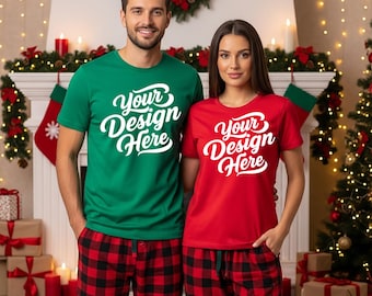 Puede incluir: Una camiseta verde y una camiseta roja, cada una con el texto "Your Design Here" en escritura blanca. Ambas personas visten pantalones de pijama a cuadros rojos y negros a juego. El fondo incluye decoraciones navideñas.