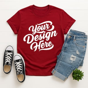 Mockup bundle featuring Gildan 64000 t-shirts in over 70+ colors. The image shows various colored t-shirts with the placeholder text 'Your Design Here' on a flat lay background with flowers, sneakers, and other accessories.