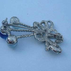 May include: Silver tone brooch with a blue glass stone and a decorative design. The brooch has a pin and catch closure.