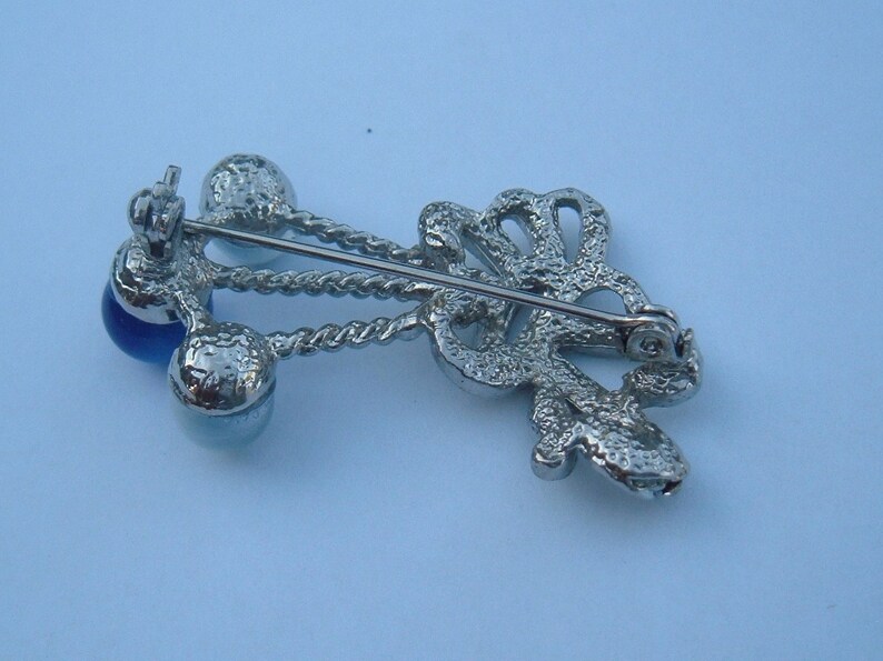 May include: Silver tone brooch with a blue glass stone and a decorative design. The brooch has a pin and catch closure.