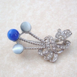 May include: A silver brooch with a blue and white stone design. The brooch features a twisted rope design with three round stones, one blue and two white.