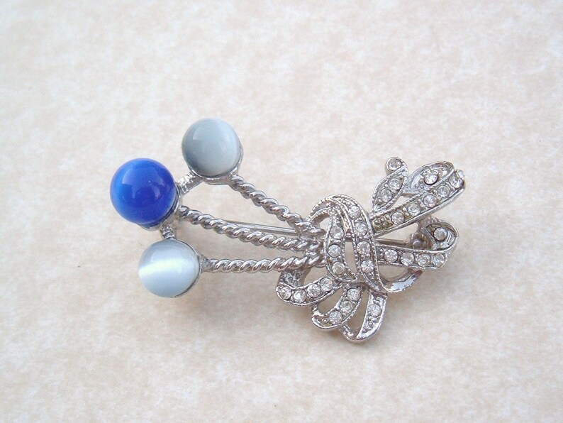 May include: A silver brooch with a blue and white stone design. The brooch features a twisted rope design with three round stones, one blue and two white.