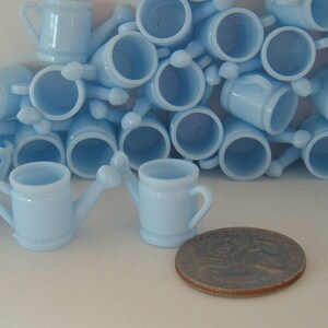 May include: A group of light blue plastic watering cans, some with handles, arranged in a pile. The watering cans are small and appear to be party favors.