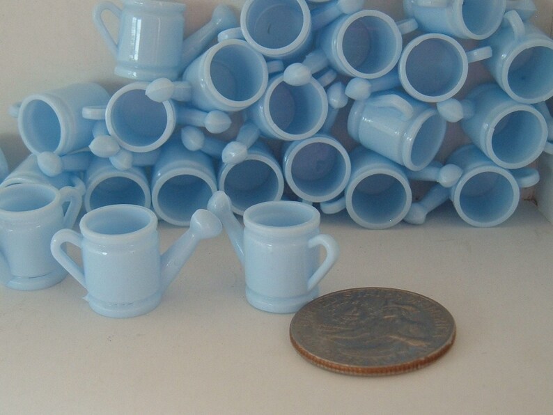May include: A group of light blue plastic watering cans, some with handles, arranged in a pile. The watering cans are small and appear to be party favors.