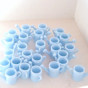 May include: A collection of light blue plastic watering cans, arranged in a circular pattern on a white surface.