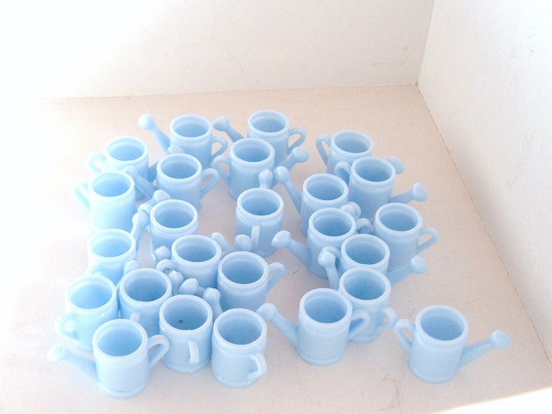 May include: A collection of light blue plastic watering cans, arranged in a circular pattern on a white surface.