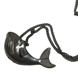 May include: A silver whale pendant necklace. The whale is detailed with a textured surface and a fin. The chain is silver and has a curb link style.