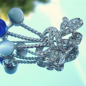 May include: A silver brooch with a bow design and clear rhinestones. The bow is accented with three round stones, two white and one blue.