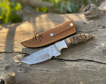 May include: A Damascus steel hunting knife with a brown horn handle and a leather sheath. The knife has a decorative pattern on the blade.