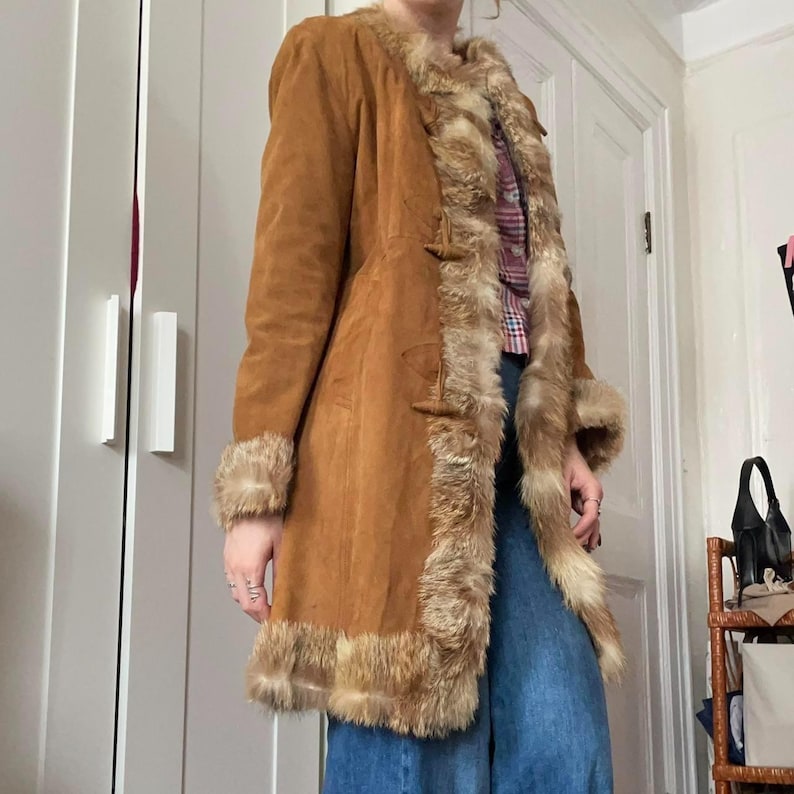 This warm and cozy Brown Suede Afghan Coat showcases stunning shaggy fur detailing that enhances its classic boho silhouette. From the textured suede to the thick trim, every detail reflects vintage craftsmanship. A must-have winter coat for anyone who loves timeless retro style and cold-weather comfort.