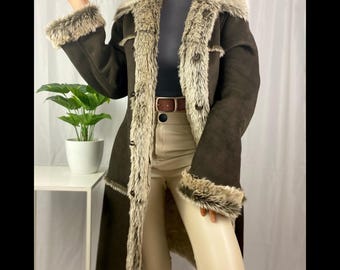 May include: A dark brown faux suede coat with faux fur trim. The coat features a longline silhouette, button closures, and fur trim around the collar, cuffs, and front edges. The coat is a vintage style.