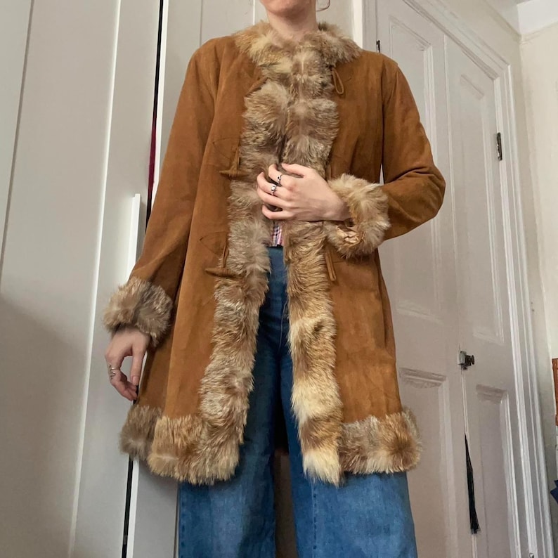 This beautiful Brown Suede Penny Lane Coat captures the essence of classic 70s Afghan fashion with its warm tan suede body and plush caramel shearling-style trim. Designed for effortless boho styling, the mid-length silhouette adds cozy winter charm while maintaining a timeless retro look. Perfect for cold days, travel, and vintage lovers seeking a statement coat.
