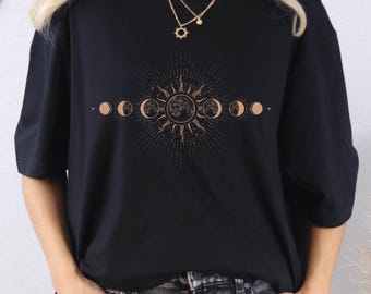 May include: Black t-shirt with a gold sun and moon phase design. The shirt has a crew neck and short sleeves. The text "BLACK" is visible in the lower right corner.