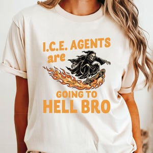 May include: A natural-colored t-shirt with the text "I.C.E. AGENTS are GOING TO HELL BRO" in orange. The graphic features a Grim Reaper riding a skateboard over flames. The word "NATURAL" is printed at the bottom left.