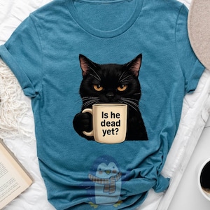 May include: A teal blue t-shirt with a black cat holding a coffee mug that says "Is he dead yet?"