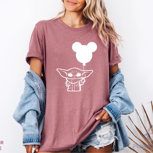 A woman wearing a pink t-shirt with a white graphic of a character and a balloon, along with a denim jacket and denim shorts.