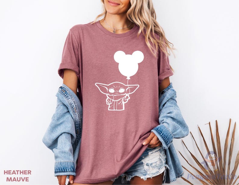 A woman wearing a pink t-shirt with a white graphic of a character and a balloon, along with a denim jacket and denim shorts.