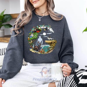 A woman wearing a gray sweatshirt with a colorful graphic design on it, sitting on a couch and holding a mug.