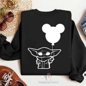 a black sweatshirt with a white graphic of a young child holding a balloon, along with a pair of sunglasses, a pair of jeans, and a pair of brown shoes.