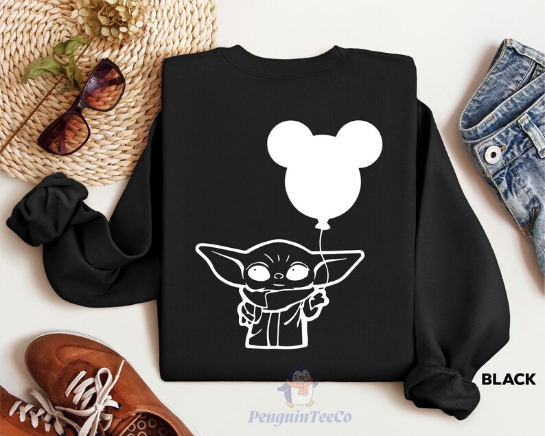 a black sweatshirt with a white graphic of a young child holding a balloon, along with a pair of sunglasses, a pair of jeans, and a pair of brown shoes.