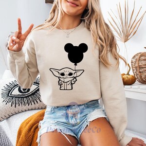 A woman wearing a sweatshirt with a graphic of a character holding a balloon is sitting in a room with various decorative items.