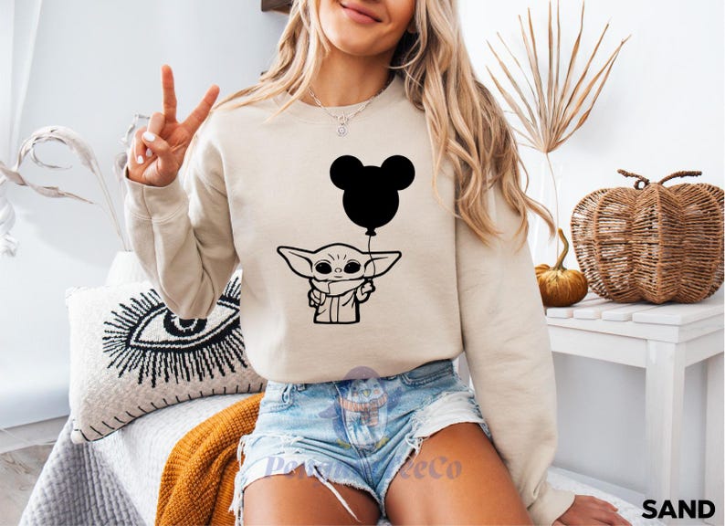 A woman wearing a sweatshirt with a graphic of a character holding a balloon is sitting in a room with various decorative items.