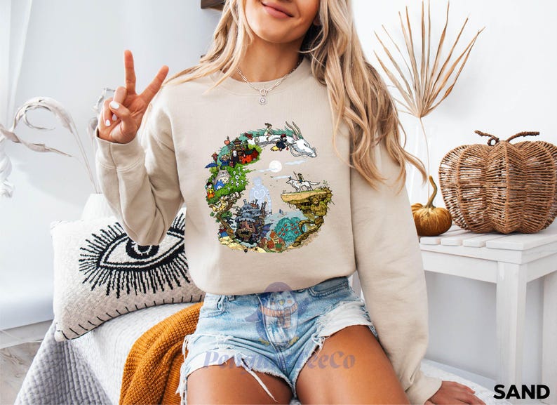 A woman wearing a sweatshirt with a graphic design of a dragon and a castle, making a peace sign with her hand.