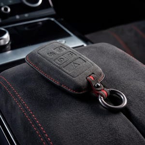 May include: A white ceramic mug with a black handle and the text "But First, Coffee" in a black, handwritten-style font. The mug is on a white surface.