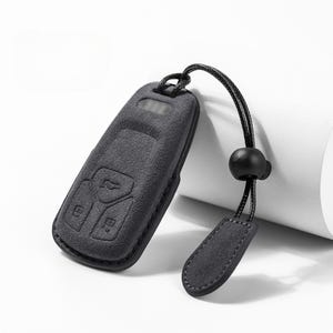 Pode incluir: Capa preta para chave do carro com superf&iacute;cie texturizada e cord&atilde;o a condizer. A capa tem bot&otilde;es em relevo e uma pequena presilha para o cord&atilde;o. O cord&atilde;o tem uma conta preta e uma pequena etiqueta retangular.
