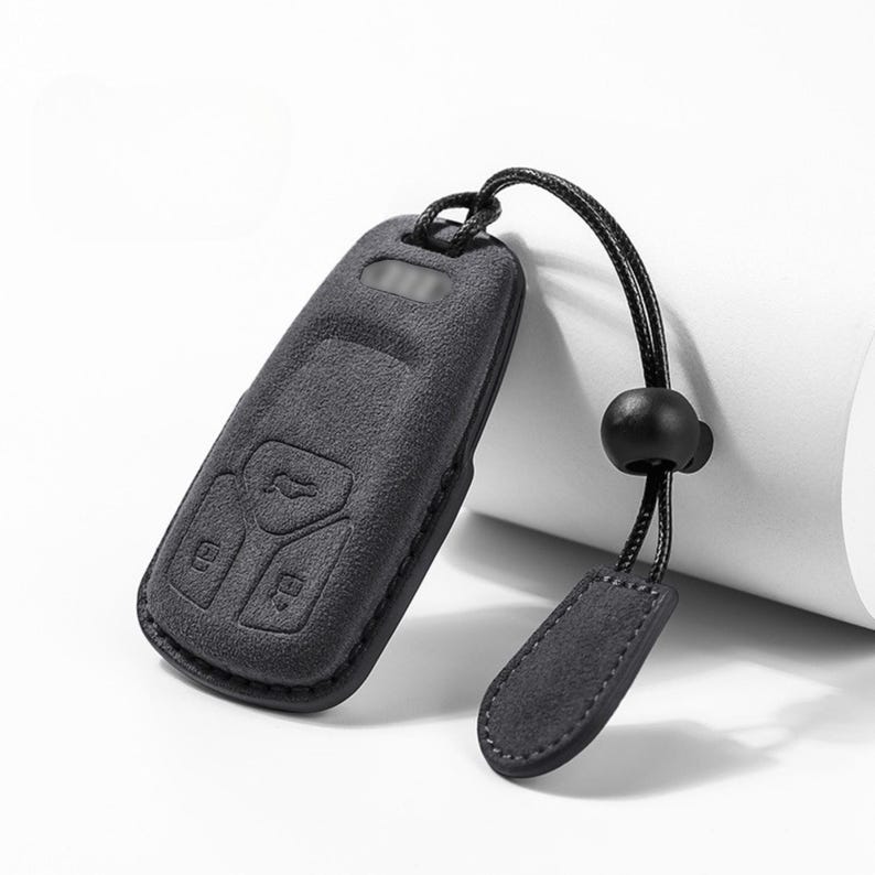 Pode incluir: Capa preta para chave do carro com superf&iacute;cie texturizada e cord&atilde;o a condizer. A capa tem bot&otilde;es em relevo e uma pequena presilha para o cord&atilde;o. O cord&atilde;o tem uma conta preta e uma pequena etiqueta retangular.