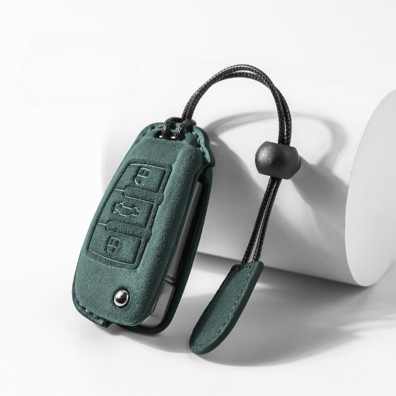 Pode incluir: Uma capa de chave de carro verde-azulado com um cord&atilde;o preto e uma conta preta. A capa tem s&iacute;mbolos de chave em relevo para trancar, destrancar e porta-malas. A capa &eacute; feita de um material macio semelhante a camur&ccedil;a.