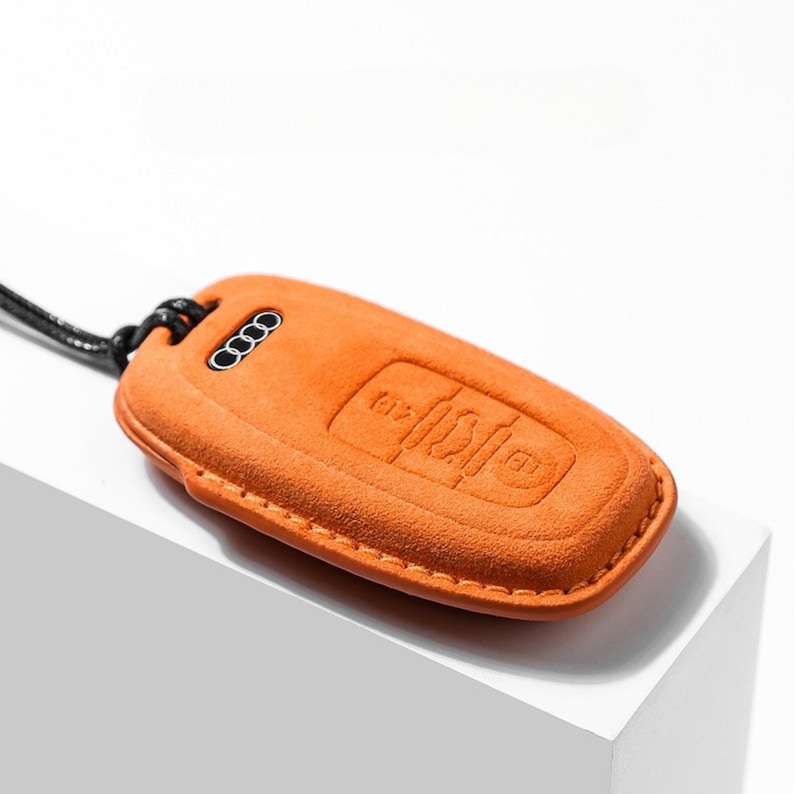 Pode incluir: Capa laranja para chave de carro com bot&otilde;es em relevo e o logotipo da Audi. A capa da chave &eacute; feita de um material semelhante a camur&ccedil;a e tem um cord&atilde;o preto preso para transporte. A capa foi projetada para proteger a chave do carro.