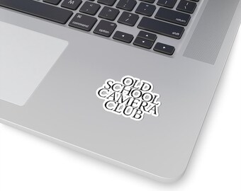 Puede incluir: Una pegatina blanca con texto negro que dice "OLD SCHOOL CAMERA CLUB" en una computadora portátil plateada.