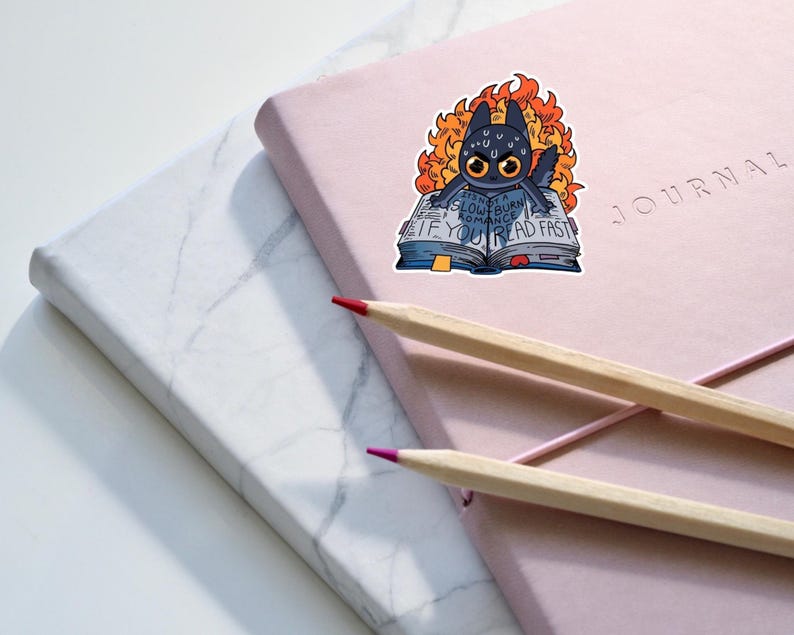 May include: A black cat with orange flames around it is reading a book that says "If you slow burn romance, you read fast".