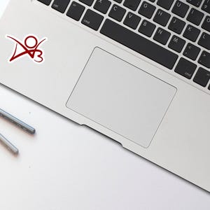 May include: A silver laptop computer with a red sticker of a stylized person with a heart on a white background. The laptop is closed and the keyboard is visible.